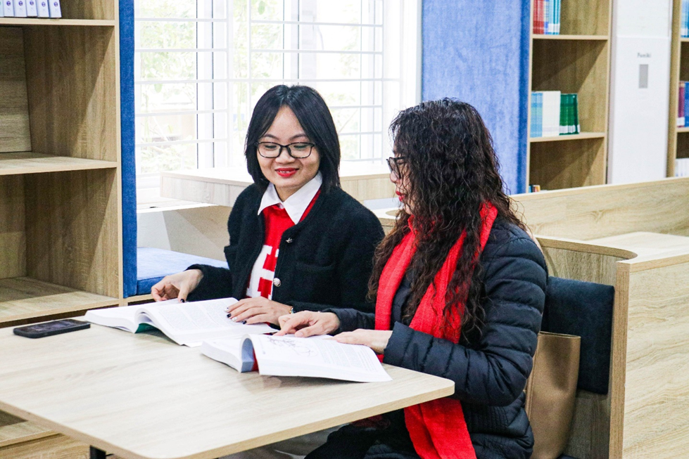 Two women sitting at a table reading books

Description automatically generated